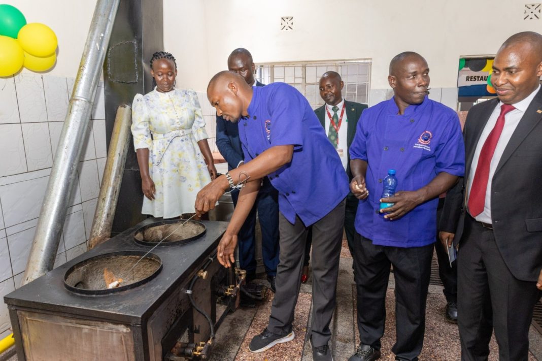 Dr. Julius Kamau, Equity Associate Director of Energy, Environment, and Climate Change (right), observes a demonstration of the redesigned cookers, now operating with gas burners in the slots previously used for wood.