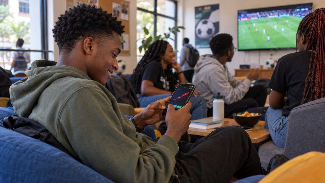 Kenyan adult exploring the Aviator crash game on a phone in an apartment common room after a match in Nairobi.
